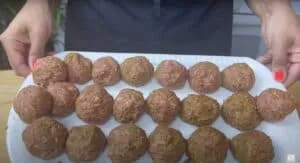 Person holding a plate of homemade meatballs ready for cooking, showcasing fresh ingredients and seasoning.